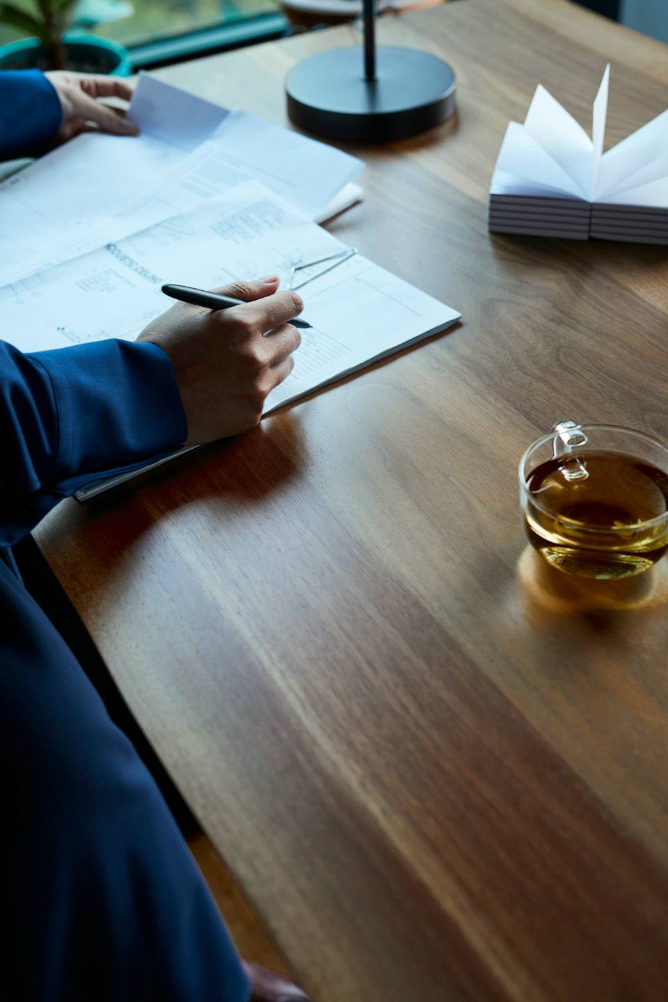 Manos con traje azul escribiendo en un documento sobre un escritorio de madera.